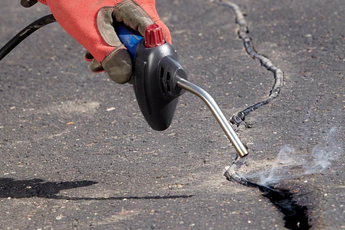 Hot rubber sealant being applied to a deep crack in an asphalt driveway